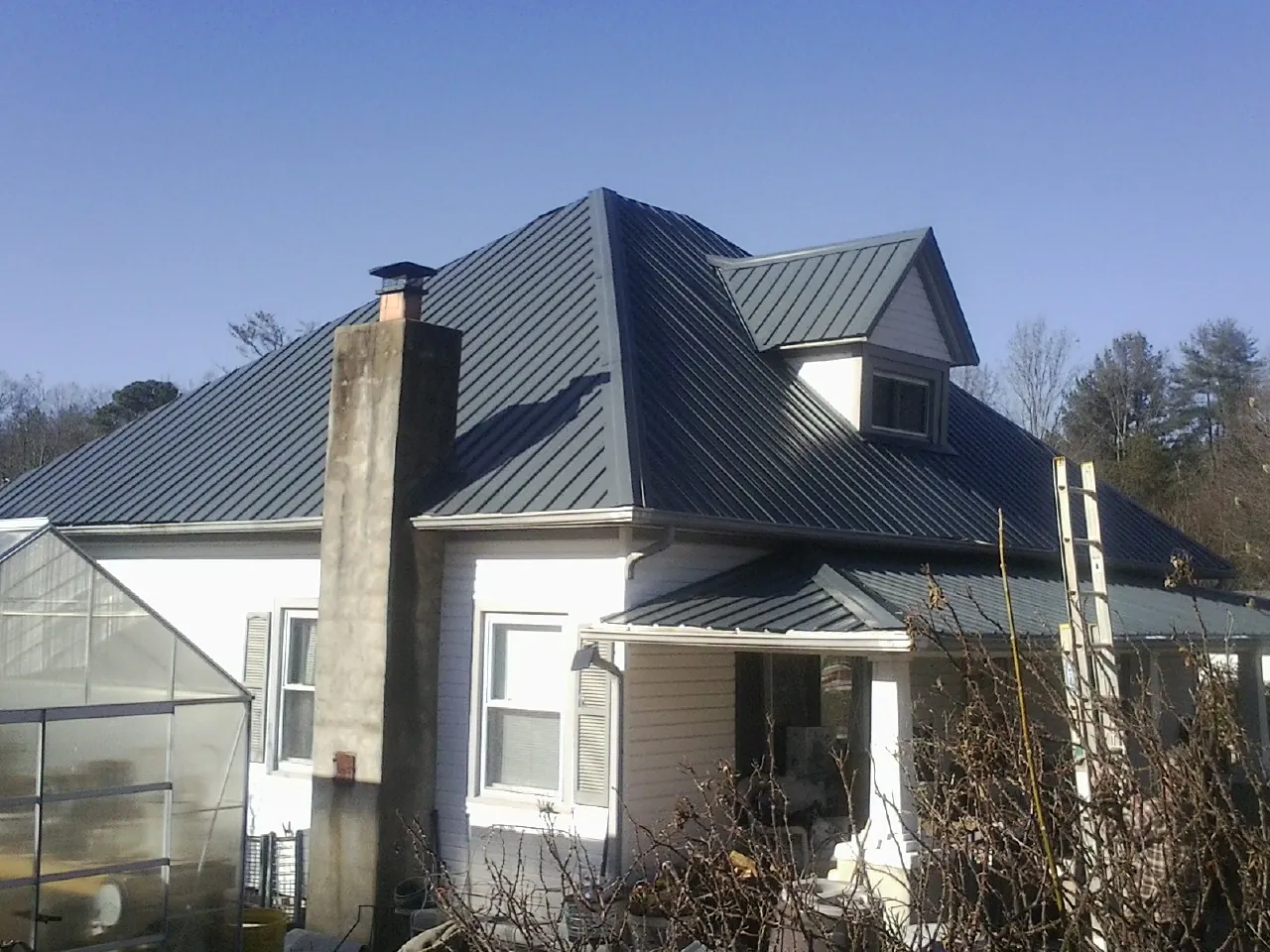 Dark blue standing seam metal roof on a white farmhouse with dormer — Slate & Tile Roof Repair by Roofing Brothers in Marine City