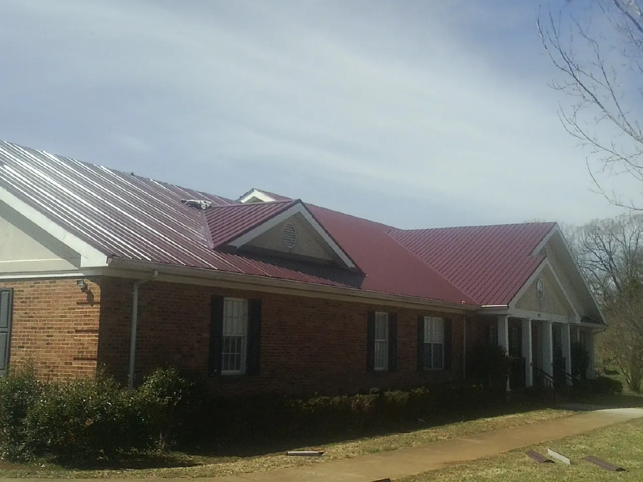 Red metal roof with gabled entries on a long brick building, from a Hail Damage Roof Repair job in Marine City
