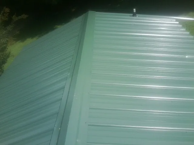 New green metal panels meeting at the ridge of a roof — Flat Roof Repair work by our crew in Marine City