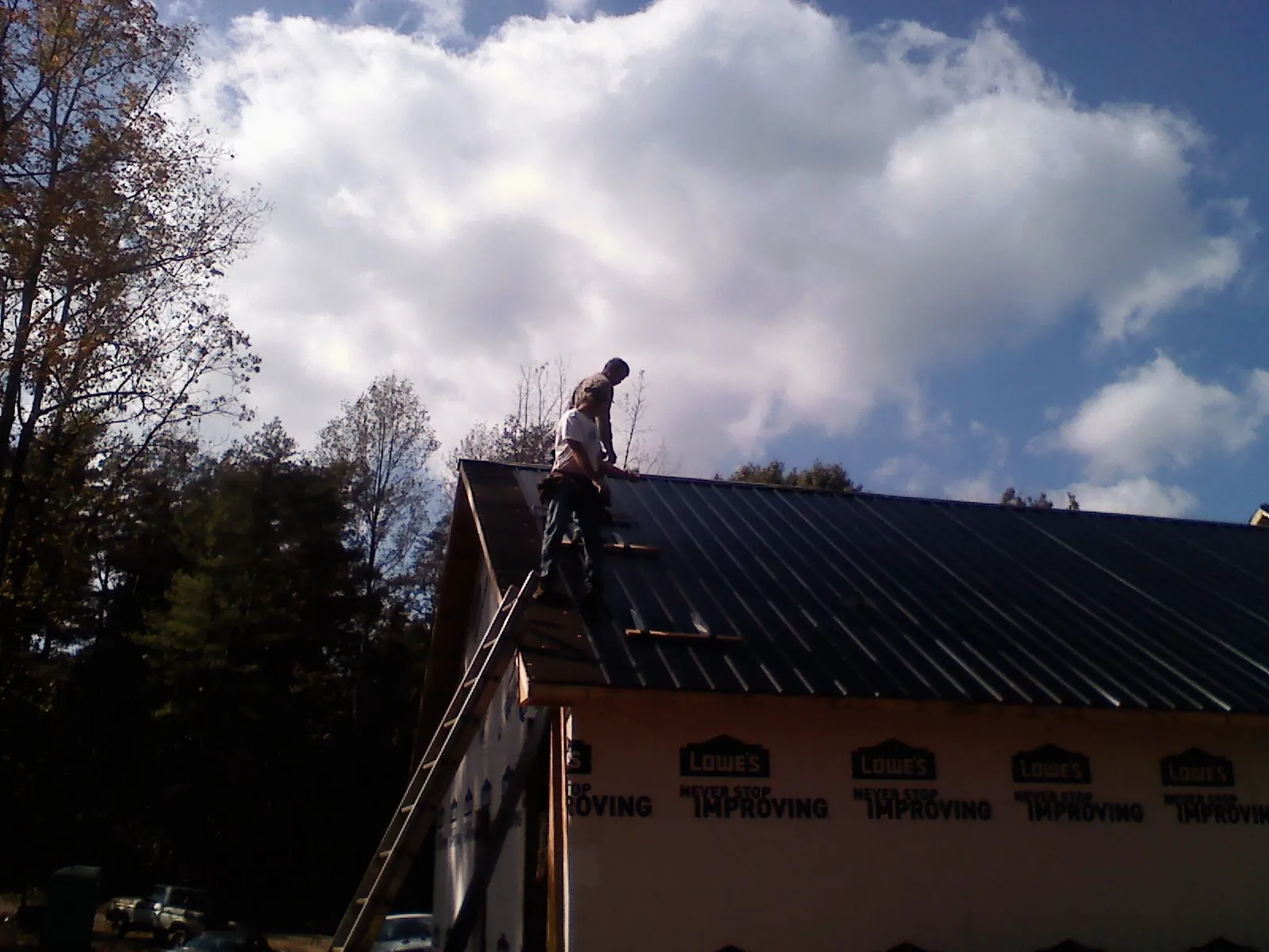 Roofer fastening dark metal panels high against a cloudy sky, from a Roof Inspection job in Marine City