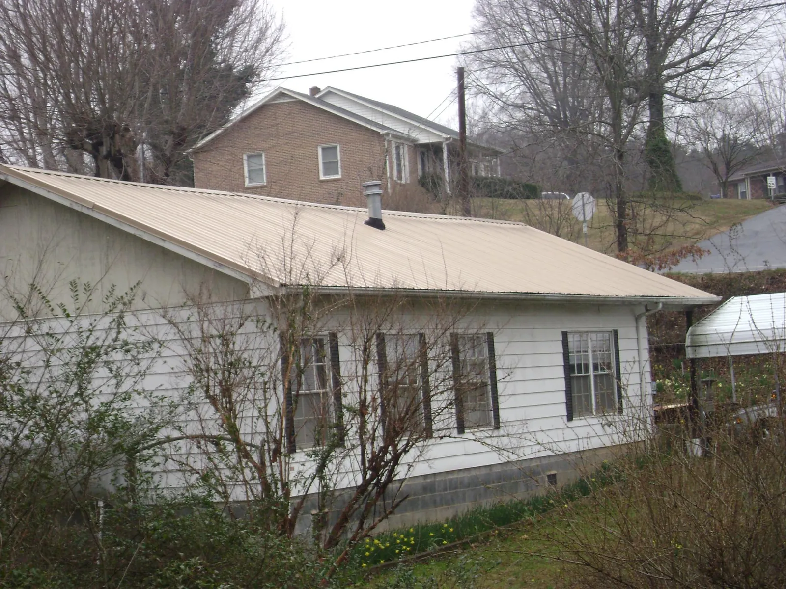 Tan metal roof on a white sided house set into a hillside — Commercial Roofing by Roofing Brothers in Marine City